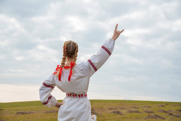 A girl in a Slavic dress with a red ribbon in her hair is standi - Photo, Image