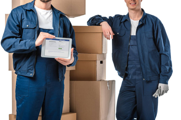 cropped view of two movers with cardboard boxes presenting digital tablet with facebook app on screen isolated on white - Фото, зображення