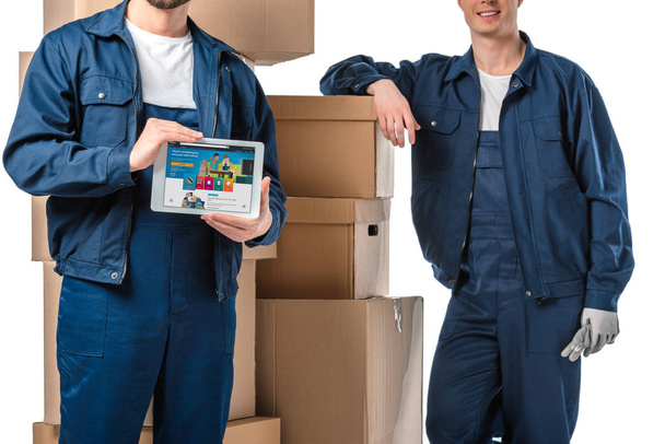 cropped view of two movers with cardboard boxes presenting digital tablet with amazon app on screen isolated on white - Foto, Imagem