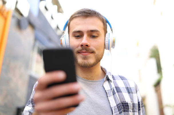 Front view of serious man listening to music walking in the street - Foto, imagen