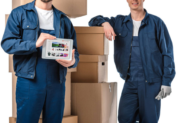 cropped view of two movers with cardboard boxes presenting digital tablet with aliexpress app on screen isolated on white - Foto, Bild