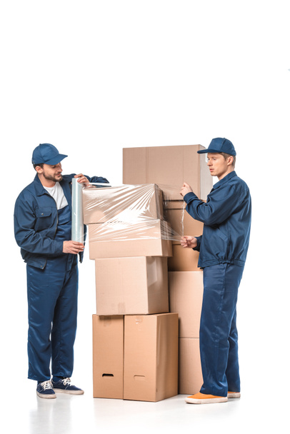 two movers wrapping cardboard boxes with roll of stretch film on white - Zdjęcie, obraz