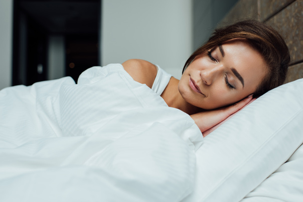 beautiful brunette woman sleeping on pillow under blanket in bed  - Фото, изображение