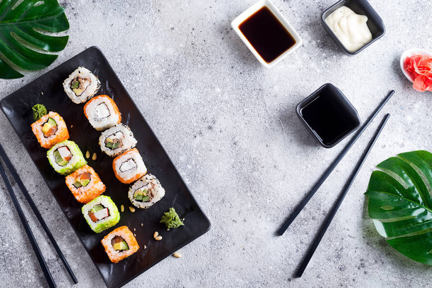 Vari sushi fresco e delizioso impostato su ardesia bianca e nera con bastoncini di metallo e ardesia, salsa e foglie verdi su sfondo pietra chiara, posa piatta
 - Foto, immagini