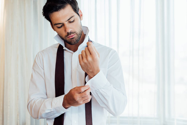 handsome bearded man touching shirt while standing in hotel  - Photo, Image