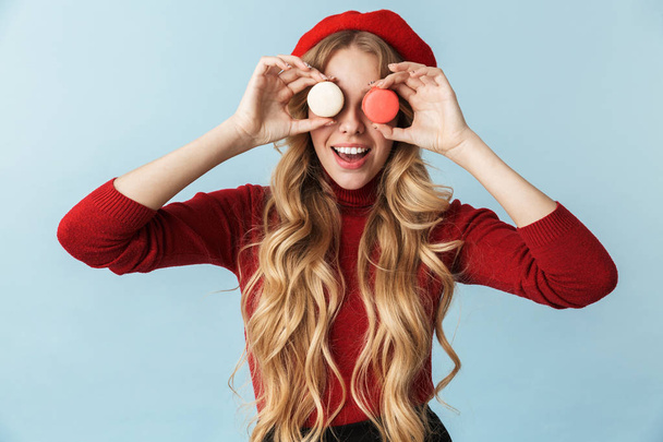 Image of cute blond woman 20s wearing red beret holding macaron  - Фото, зображення