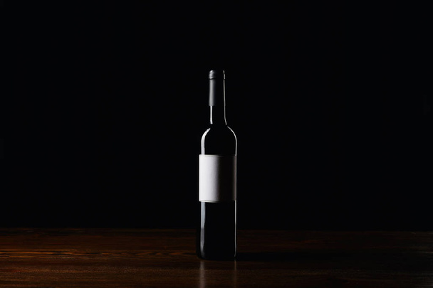 Wine bottle with blank label on wooden surface isolated on black - Φωτογραφία, εικόνα