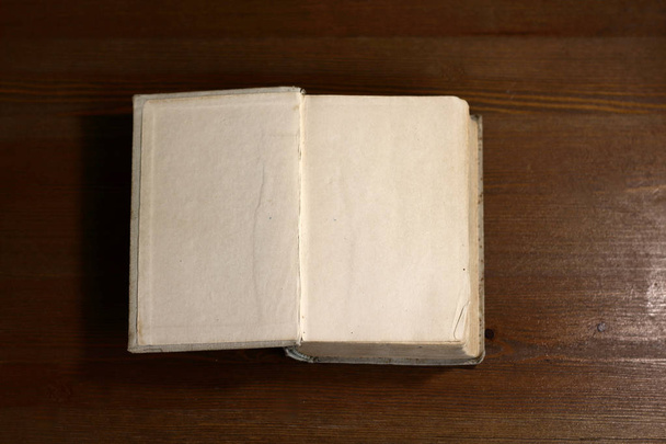 An open old retro book with white empty blank pages on which the designer can write a greeting text or a postcard on the wooden background of the library atmosphere - Photo, Image