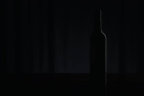 Silhouette of wine bottle on black surface on dark - Foto, imagen