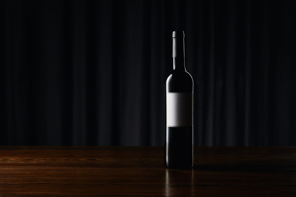 Wine bottle with blank label on wooden surface on dark - 写真・画像