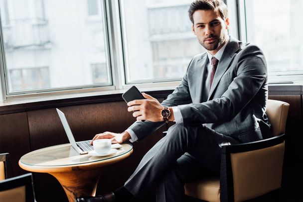 handsome bearded businessman holding smartphone while using laptop  - Foto, immagini