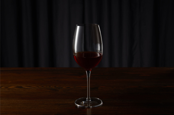 Glass with red wine on wooden surface on dark - Фото, изображение