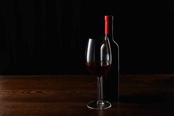 Bottle and glass of red wine on wooden surface isolated on black - Foto, imagen
