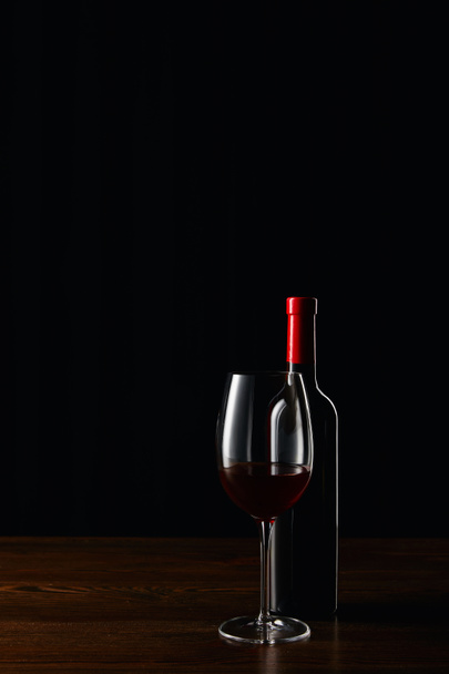 Bottle and glass of red wine on wooden surface isolated on black - Foto, immagini