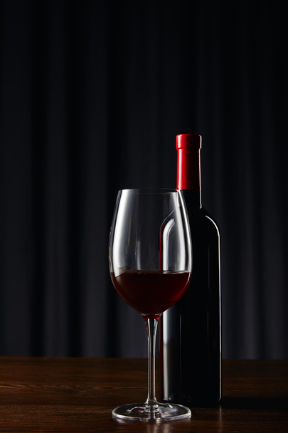 Bottle and glass of red wine on wooden surface on dark - Φωτογραφία, εικόνα