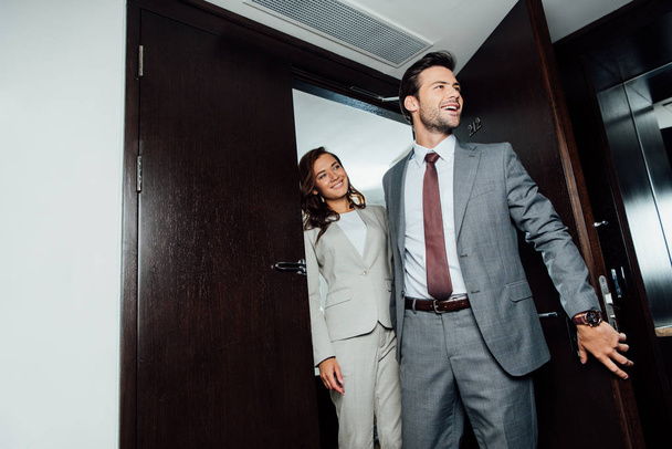 cheerful bearded man and attractive woman in formal wear entering hotel room  - Фото, изображение