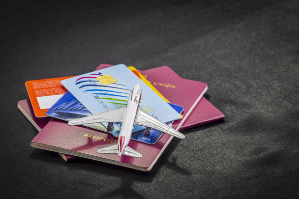 Flugzeugmuster auf internationalen Pässen, Kreditkarten und Koffern auf schwarzem Hintergrund. Vorbereitung eines Flugzeugfluges und die notwendigen Dokumente und Mittel dazu. - Foto, Bild
