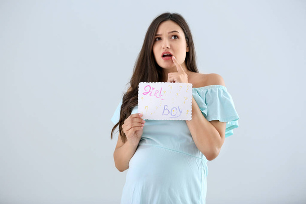 Emotional pregnant woman holding paper with text "BOY? GIRL?" on light background - Foto, immagini