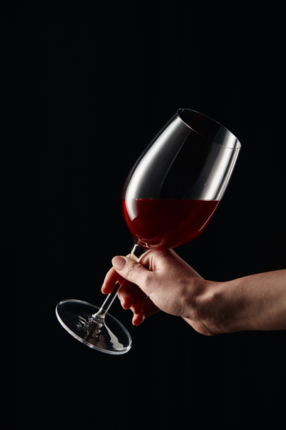Cropped view of woman holding wine glass with red wine isolated on black - Фото, изображение