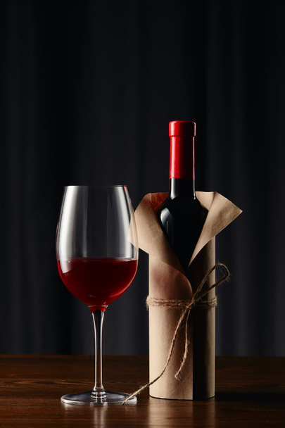 Wine glass and bottle in paper wrapper on wooden surface - Foto, imagen