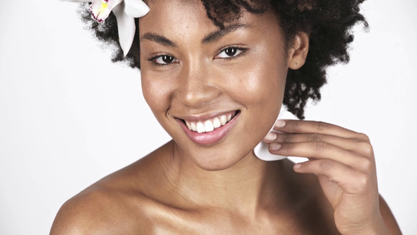 alegre afroamericana mujer sosteniendo algodón almohadilla y limpieza cara y cuello en blanco
  - Imágenes, Vídeo