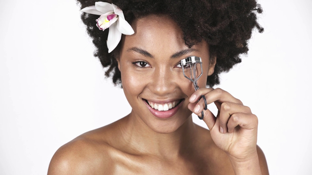 attractive african american woman smiling and using eyelash curler on white  - Video, Çekim