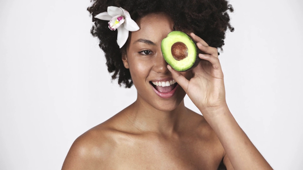 piękne nagie african american dziewczyna patrząc na połówki Avocado, uśmiechając się i obejmujące oko na biały  - Materiał filmowy, wideo