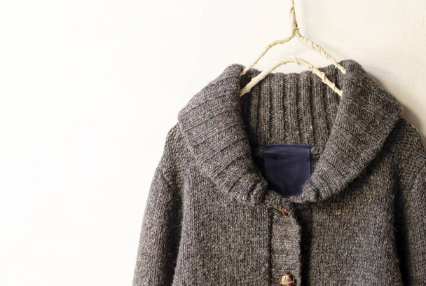 a thick knitted cardigan in brown hanging on clothes hanger on white background. - 写真・画像