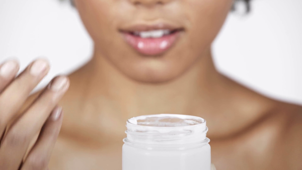 vista recortada da mulher americana africana que toma o creme cosmético do recipiente e sorrindo isolado no branco
  - Filmagem, Vídeo