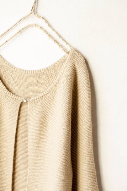 a cardigan in beige hanging on clothes hanger on white background. - 写真・画像