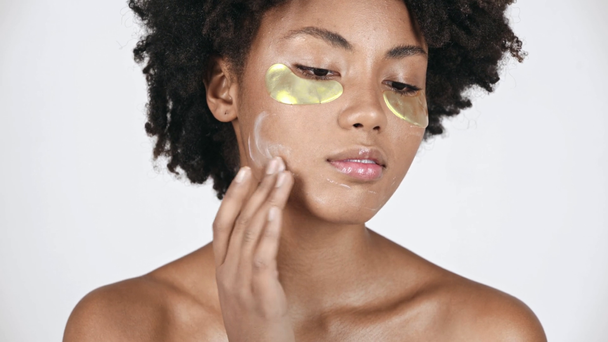 mooi Afro-Amerikaanse meisje oog patches kijken container, gezichtscrème, nemen toe te passen op gezicht en glimlachend op wit  - Video