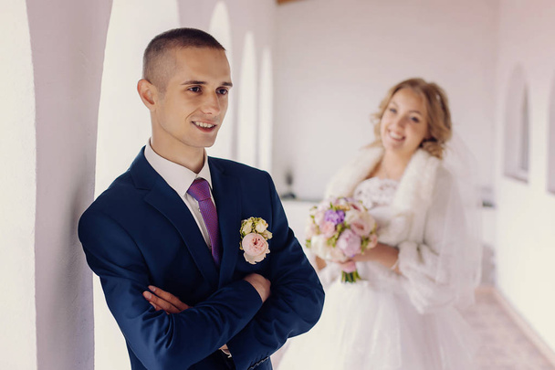 Handsome young man stands in the interior. His bride is standing on a blurred background. - Foto, immagini