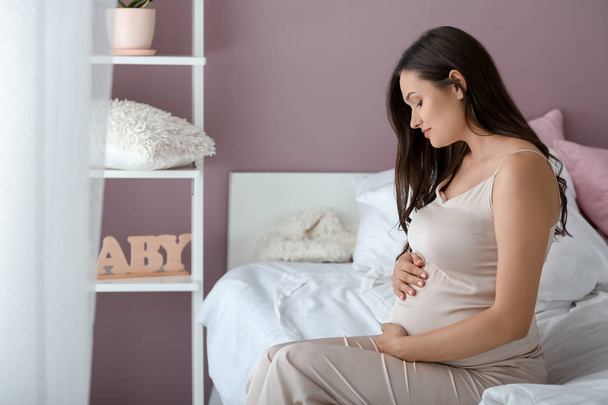 Kaunis raskaana oleva nainen istuu sängyssä
 - Valokuva, kuva