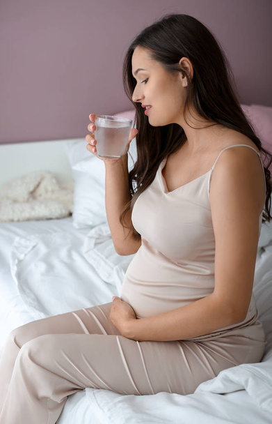 Bela mulher grávida bebendo água no quarto
 - Foto, Imagem