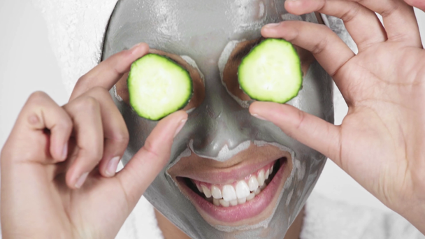 close up de mulher americana africana alegre em máscara de barro sorrindo, cobrindo os olhos com fatias de pepino e rindo isolado em branco
  - Filmagem, Vídeo