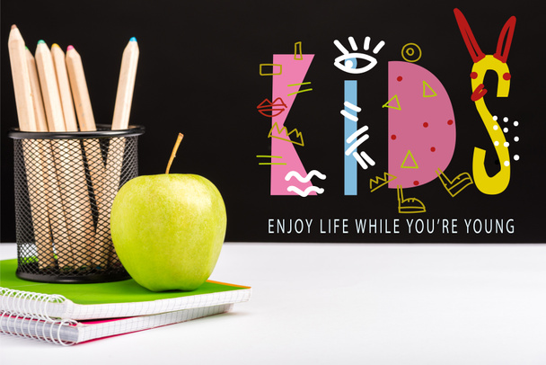pomme verte, cahiers et crayons de couleur sur la table avec profiter de la vie pendant que vous êtes jeune et les enfants lettrage sur noir
  - Photo, image