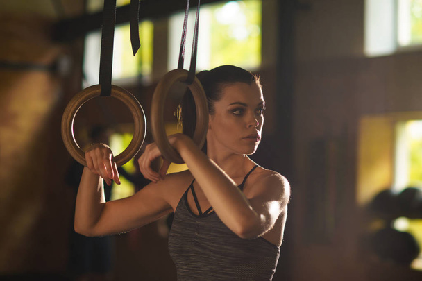 Fit, sporty and athletic sportswoman working in a gym. Woman training using gymnastic rings. Sports, lifestyle, athletics and fitness concept. - Foto, Imagen