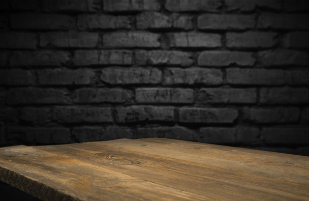 Enfoque seleccionado mesa de madera marrón vacía y textura de pared o imagen de fondo borrosa de pared de ladrillo negro viejo. para su fotomontaje o visualización del producto - Foto, Imagen
