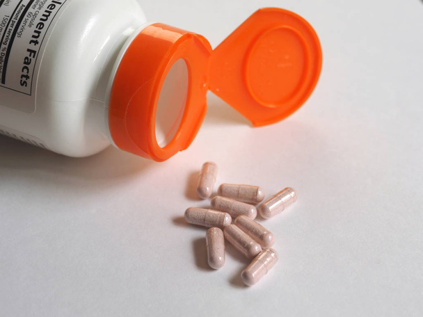 Рассеянные таблетки из аптечной бутылки и горсть капсул на белом фоне
. - Фото, изображение