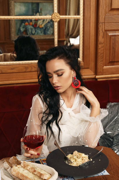 sensual woman with dark hair in elegant clothes and earrings sit - Foto, afbeelding