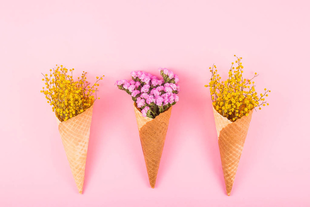 Pink and yellow flowers in waffle cones for ice cream on a bright background. Top view, flat lay - Photo, Image