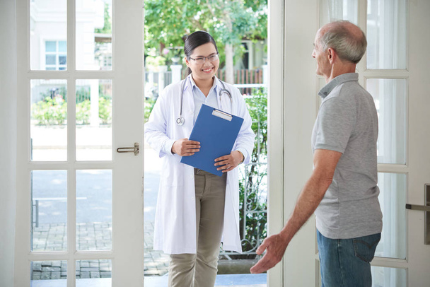 Elderly man opening door to smiling doctor making visit at home - Photo, Image