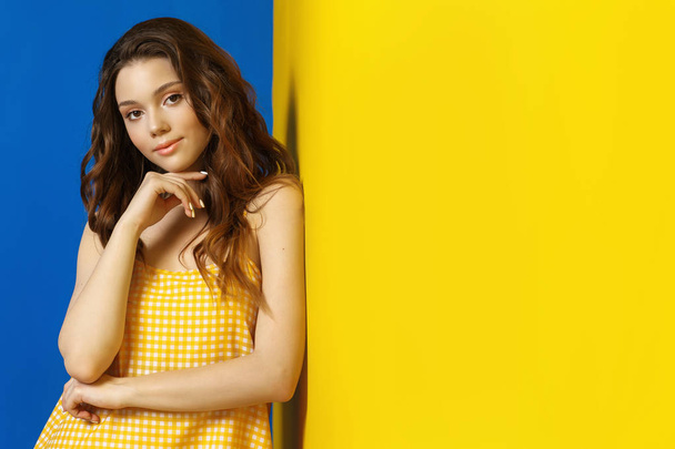 Young woman in yellow sarafan posing near blue background - Фото, изображение