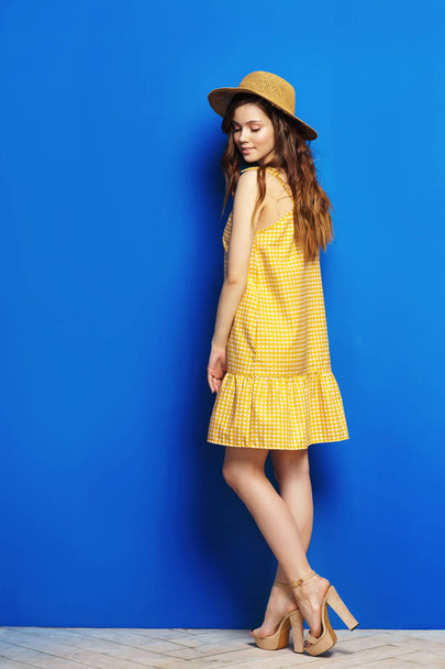 Young woman in yellow sarafan posing near blue background - Foto, afbeelding