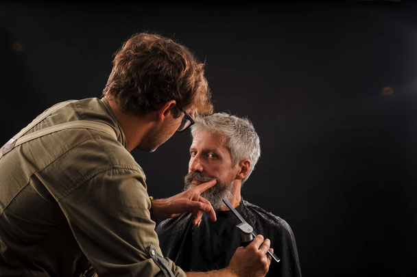 перукар розрізає бороду клієнту на літнього сивого чоловіка
 - Фото, зображення