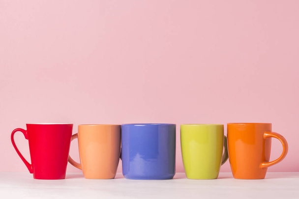 A lot of multicolored cups of coffee or tea on a pink background. The concept of a friendly company, a large family, meeting friends for a cup of tea or coffee. - Photo, Image