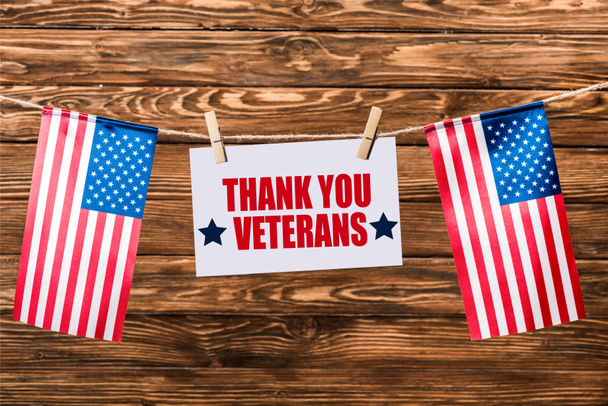 tarjeta con letras de agradecimiento veteranos colgando de la cadena con alfileres y banderas americanas sobre fondo de madera
 - Foto, Imagen