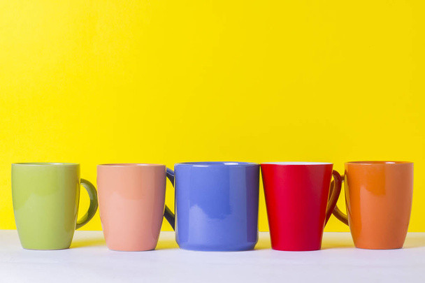 A lot of multicolored cups of coffee or tea on a yellow background. The concept of a friendly company, a large family, meeting friends for a cup of tea or coffee. - Photo, Image