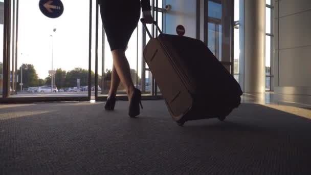 Деловая леди покидает аэропорт через автоматическую стеклянную дверь со своим багажом. Молодая женщина на каблуках идет от терминала и катает чемодан на колесах. Концепция рабочей поездки или путешествия. Медленное движение
 - Кадры, видео