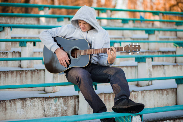 Młody mężczyzna siedzący na schodach, gra na gitarze i śpiew, muzyka koncepcja - Zdjęcie, obraz